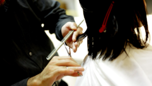 A hairstylist's hands cutting a person's black, shoulder-length hair.